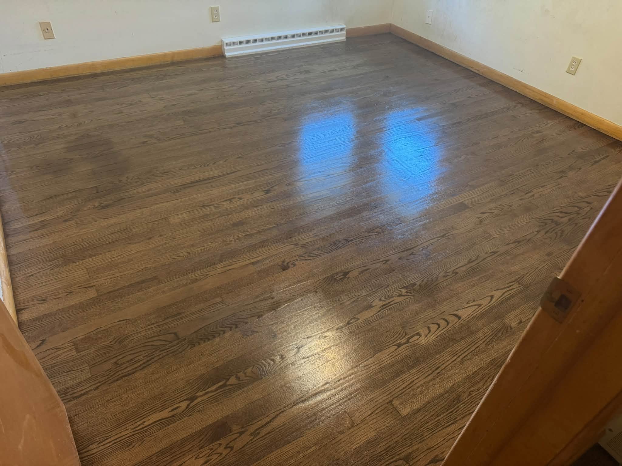 The same hardwood floor after refinishing, seen from the doorway with a darker glossy finish