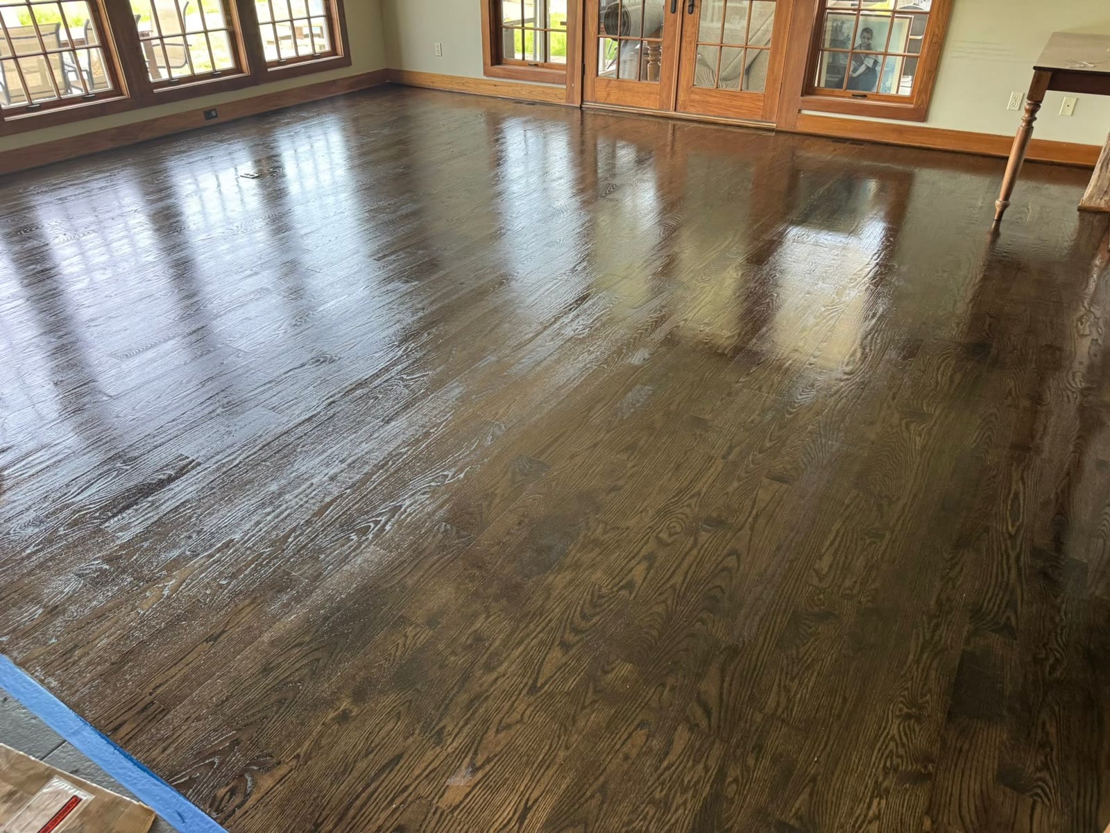 The same room after refinishing, with a darker glossy hardwood floor, wood windows, and French doors