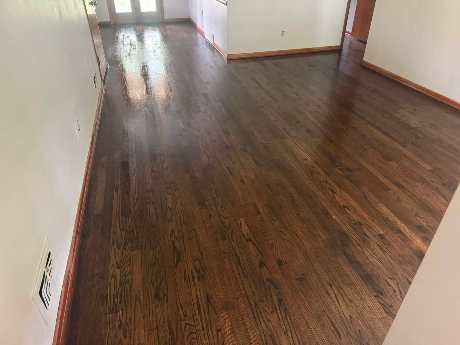 The same open room after refinishing, with a darker glossy hardwood floor, wood baseboards, and French doors