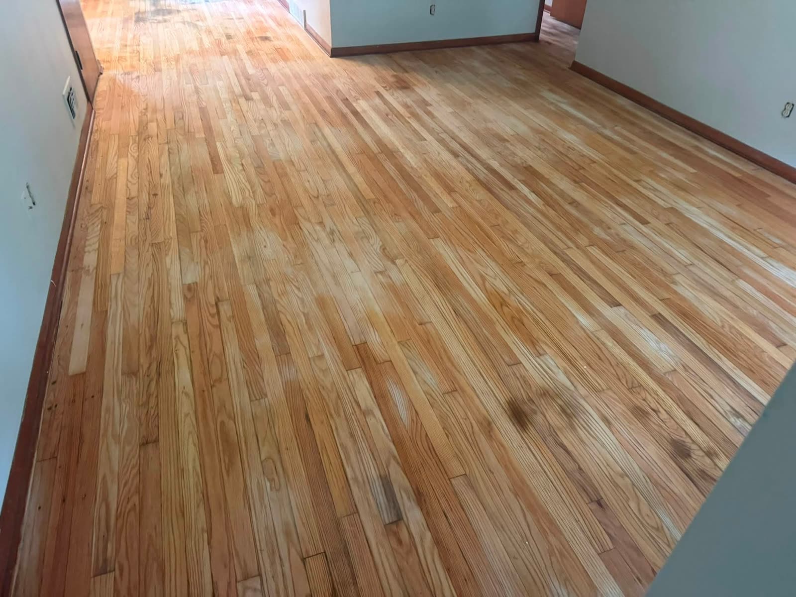 Light hardwood floor in an open room with wood baseboards, a doorway, and a floor vent